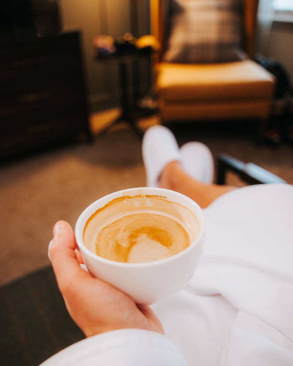 Person holding coffee watching TV in a hotel room in the Main Lodge at The Highlands