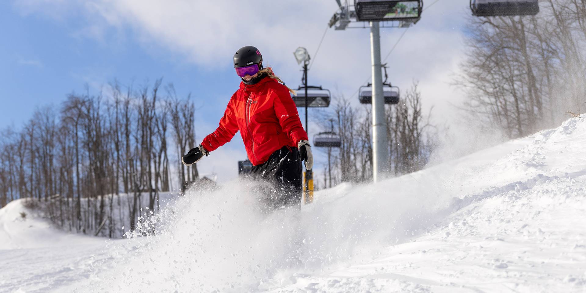 A snowboarder in powder under Camelot 6 chairlift at The Highlands